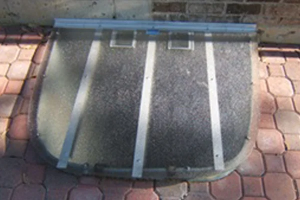 Clear polycarbonate window well cover installed on a galvanized well against a brick home